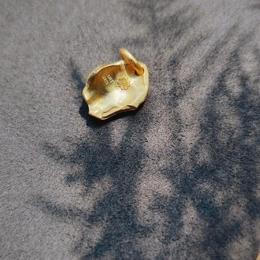 Small gold pendant with textured surface and loop on gray fabric background
