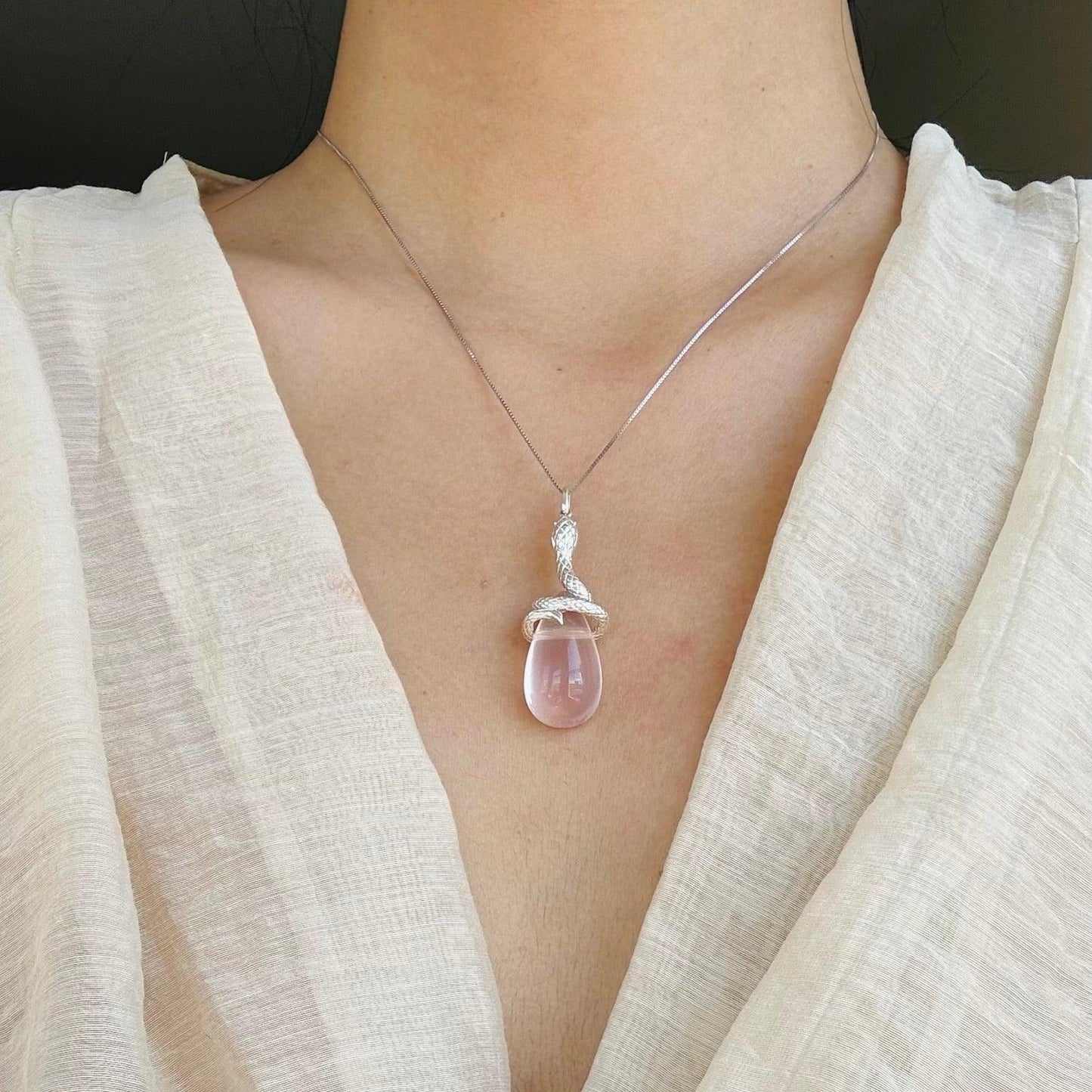 Close-up of a silver snake pendant necklace with rose quartz stone worn with a cream V-neck top