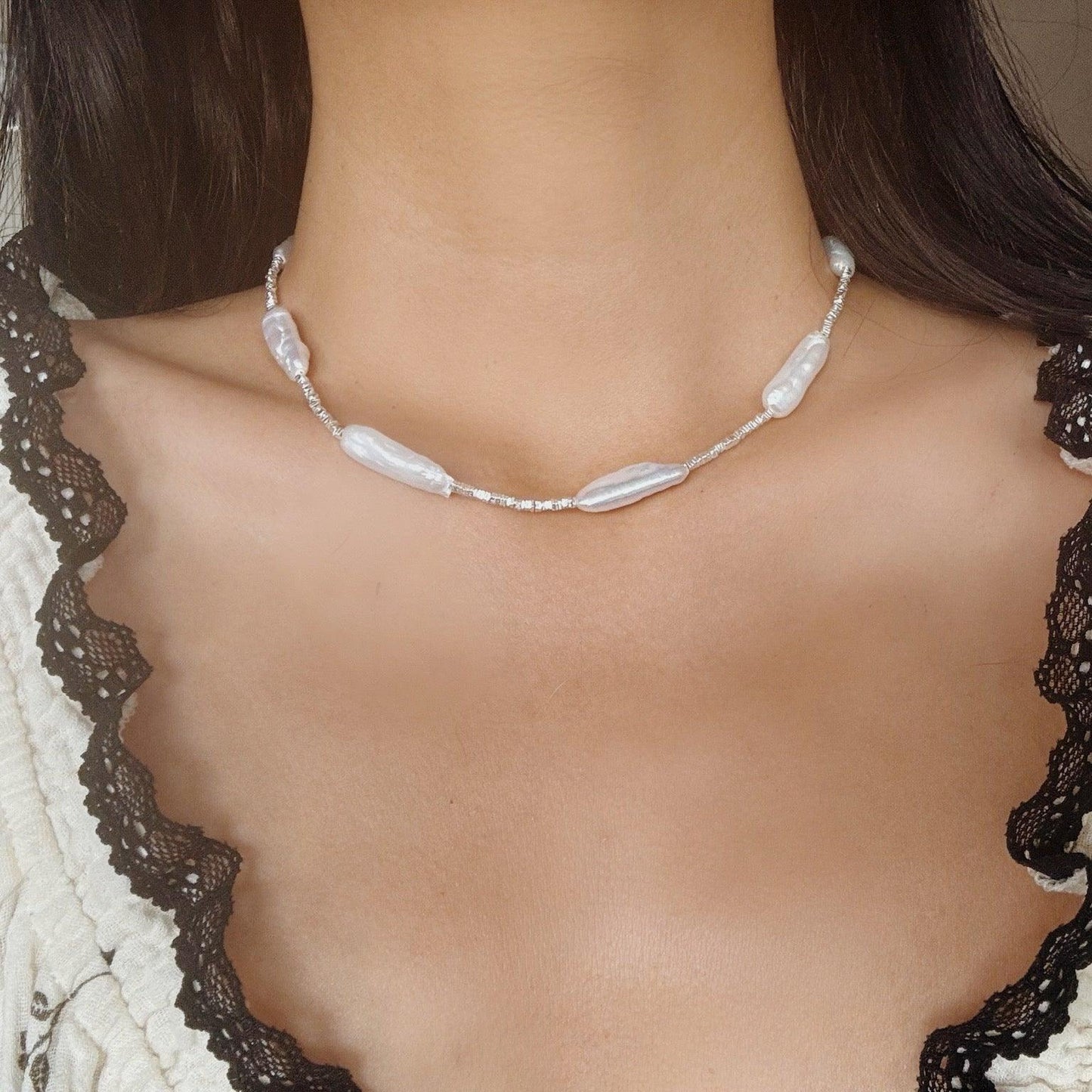 Baroque irregular pearl and silver beaded necklace worn with lace-trimmed cream and black top