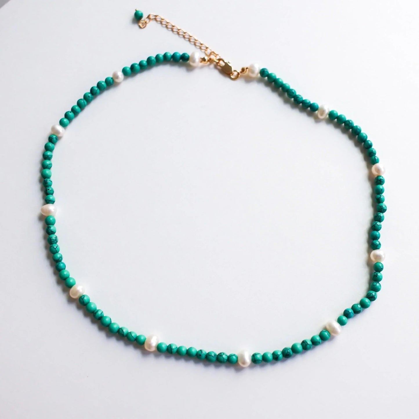 Turquoise beaded necklace with scattered white pearls and gold clasp on white background