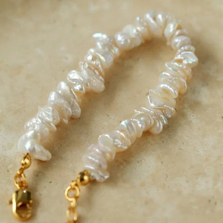 Baroque pearl bracelet with irregular white pearls and gold clasp on beige surface