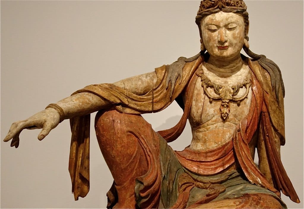 ancient seated Buddha statue with intricate robes and serene expression in museum display