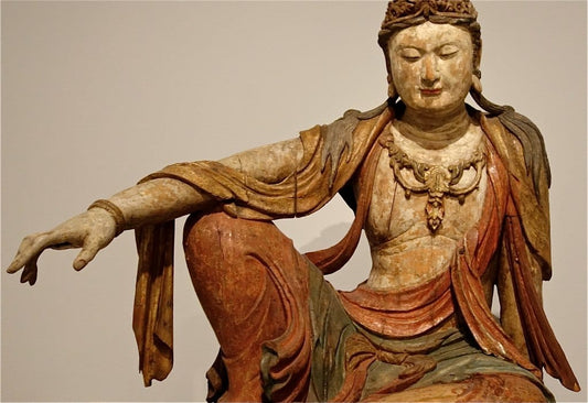 ancient seated Buddha statue with intricate robes and serene expression in museum display