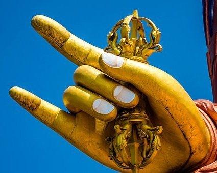 Golden hand of Buddha statue holding ornate vajra against clear blue sky