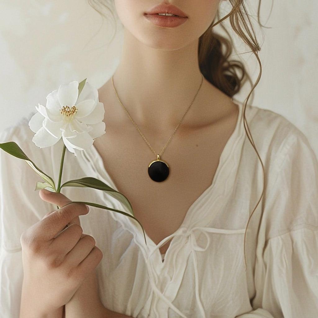 Close-up of woman in white blouse holding white flower and wearing black pendant necklace