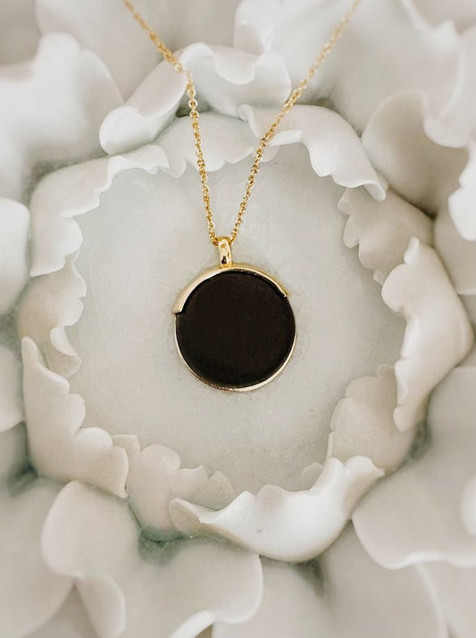 Gold necklace with round black pendant placed on white flower petals, elegant jewelry close-up