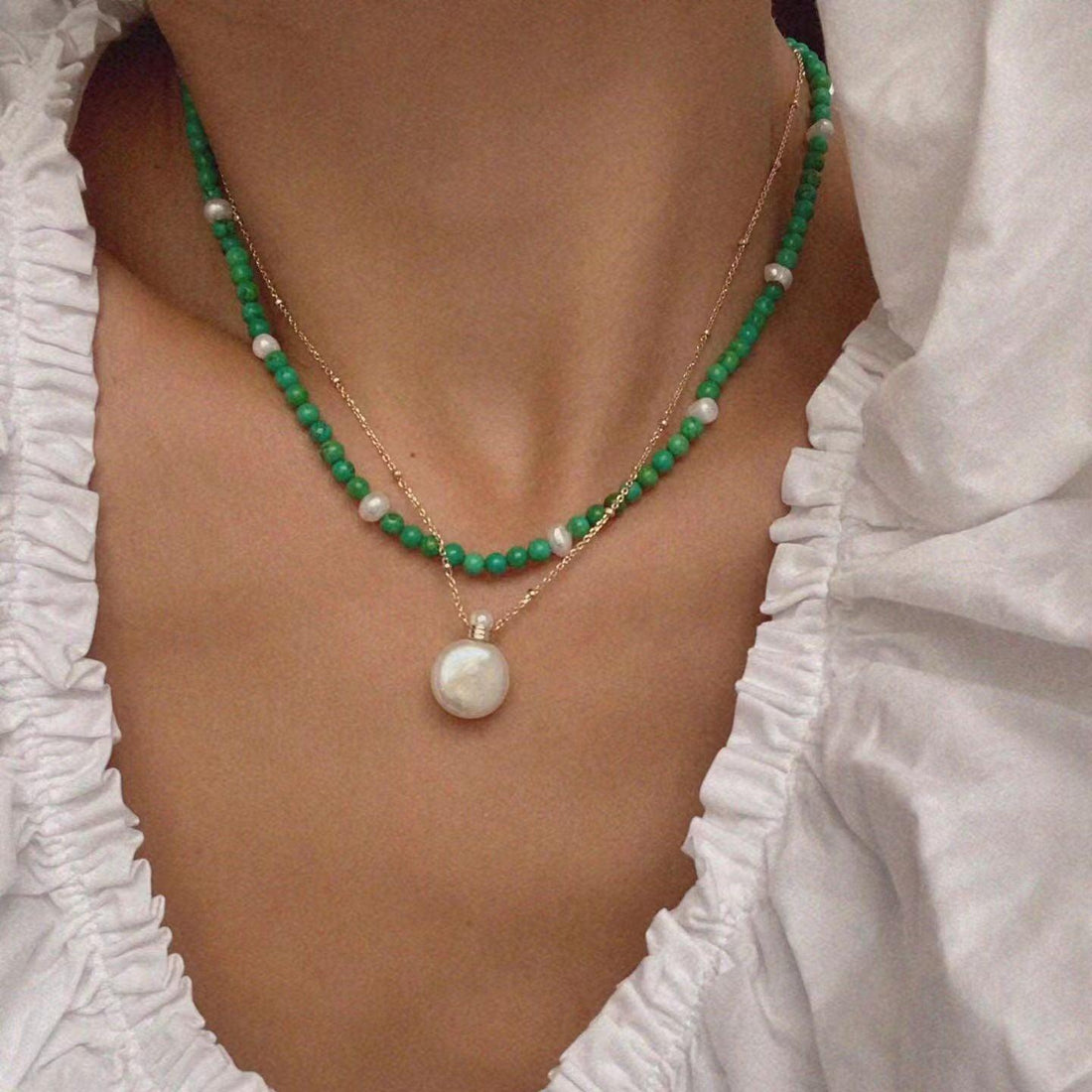 Close-up of layered turquoise bead necklace with pearl accents and a gold chain with pearl pendant