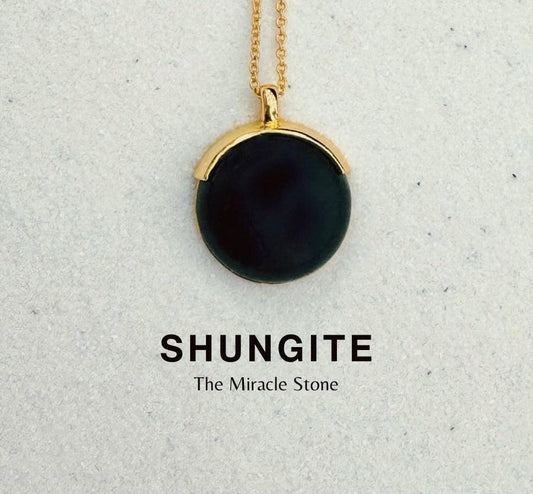 Black shungite pendant with gold setting on light background, labeled 'SHUNGITE The Miracle Stone'