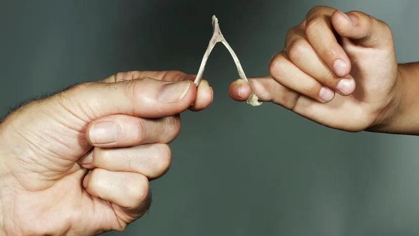 Close-up of two hands holding and crossing a wishbone against a gray background