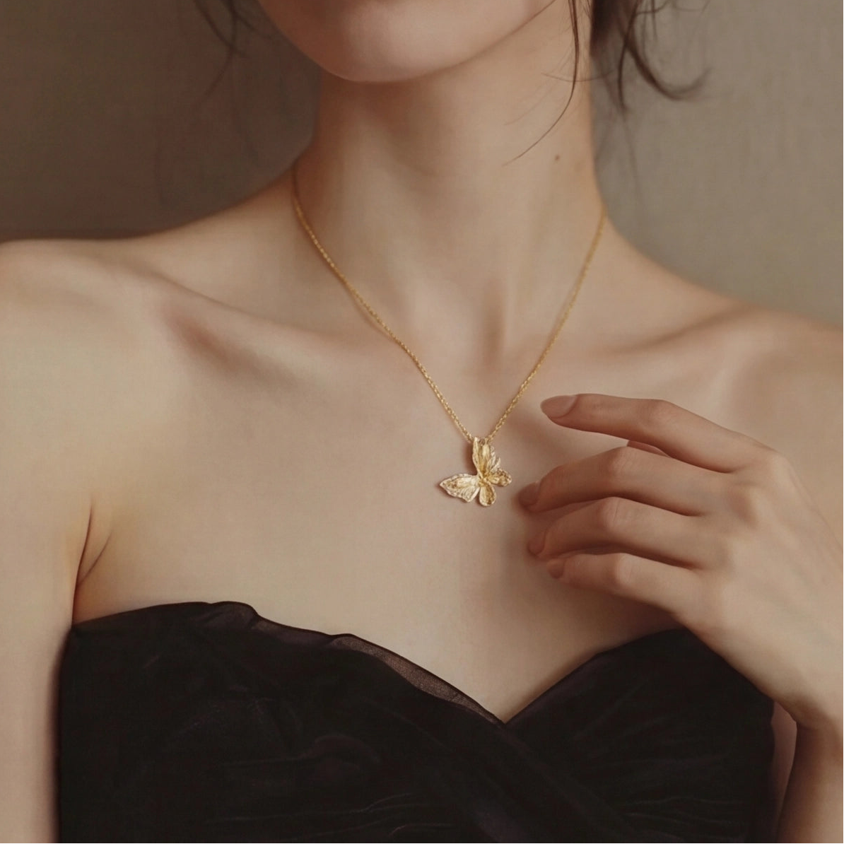 Woman wearing a gold necklace with a butterfly pendant, holding it with her hand.