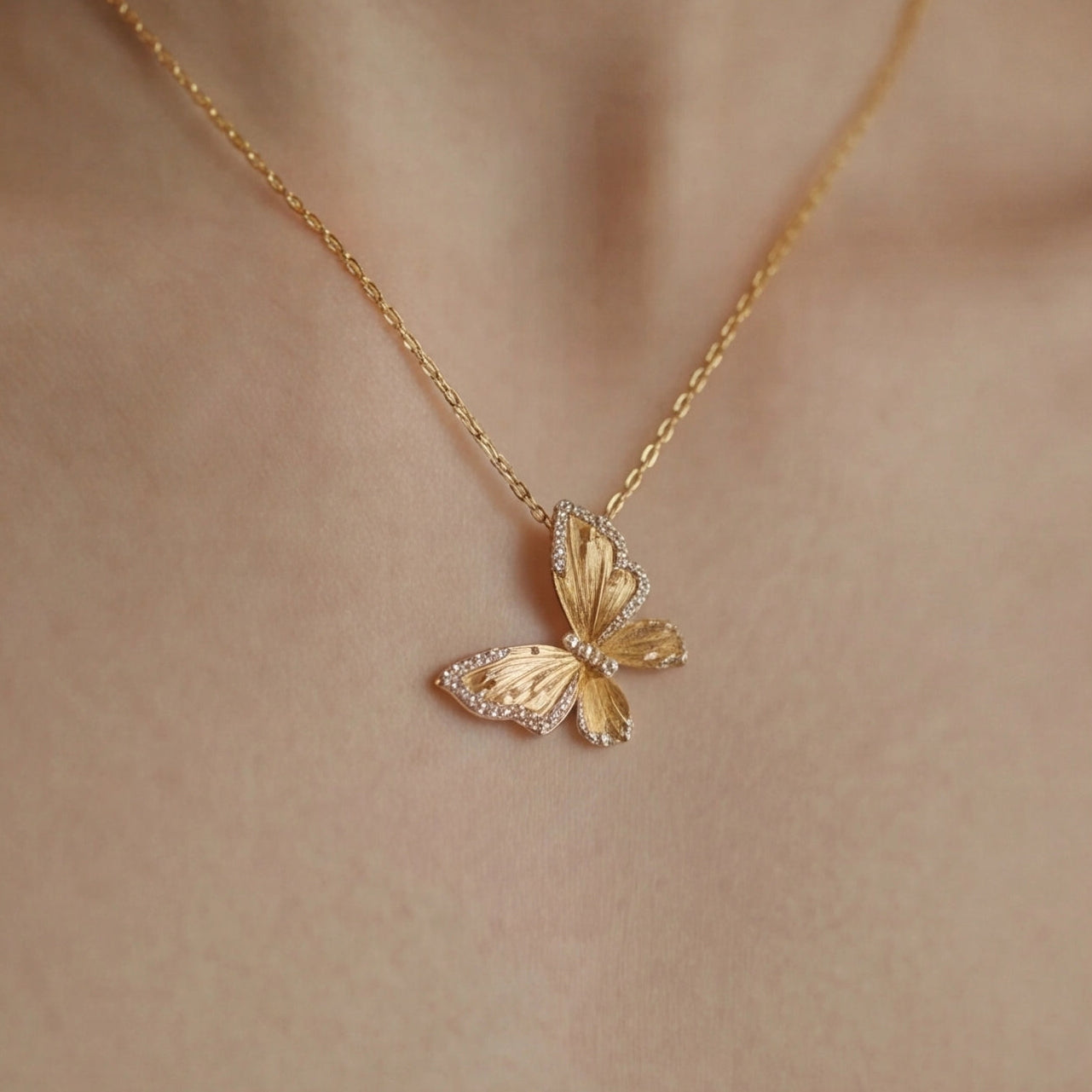 Gold butterfly necklace on a person's neck against a neutral background
