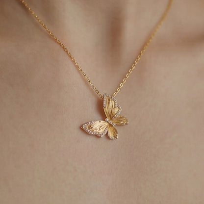 Gold butterfly necklace on a person's neck against a neutral background
