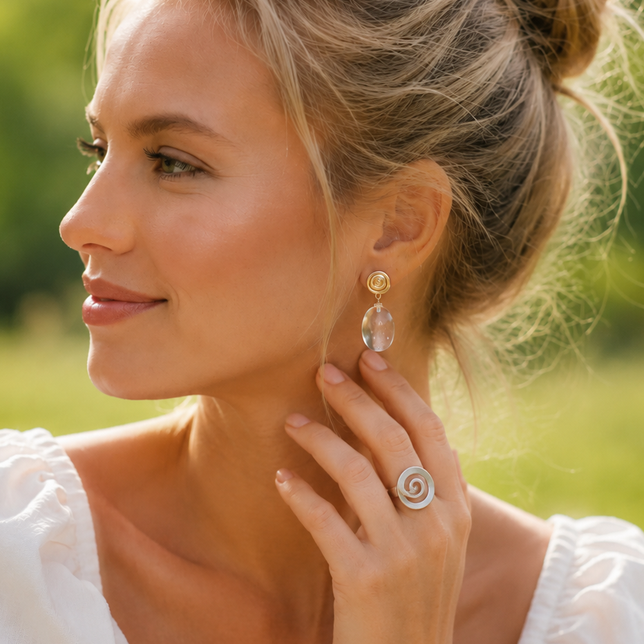 Woman wearing earrings and a ring outdoors with greenery in the background