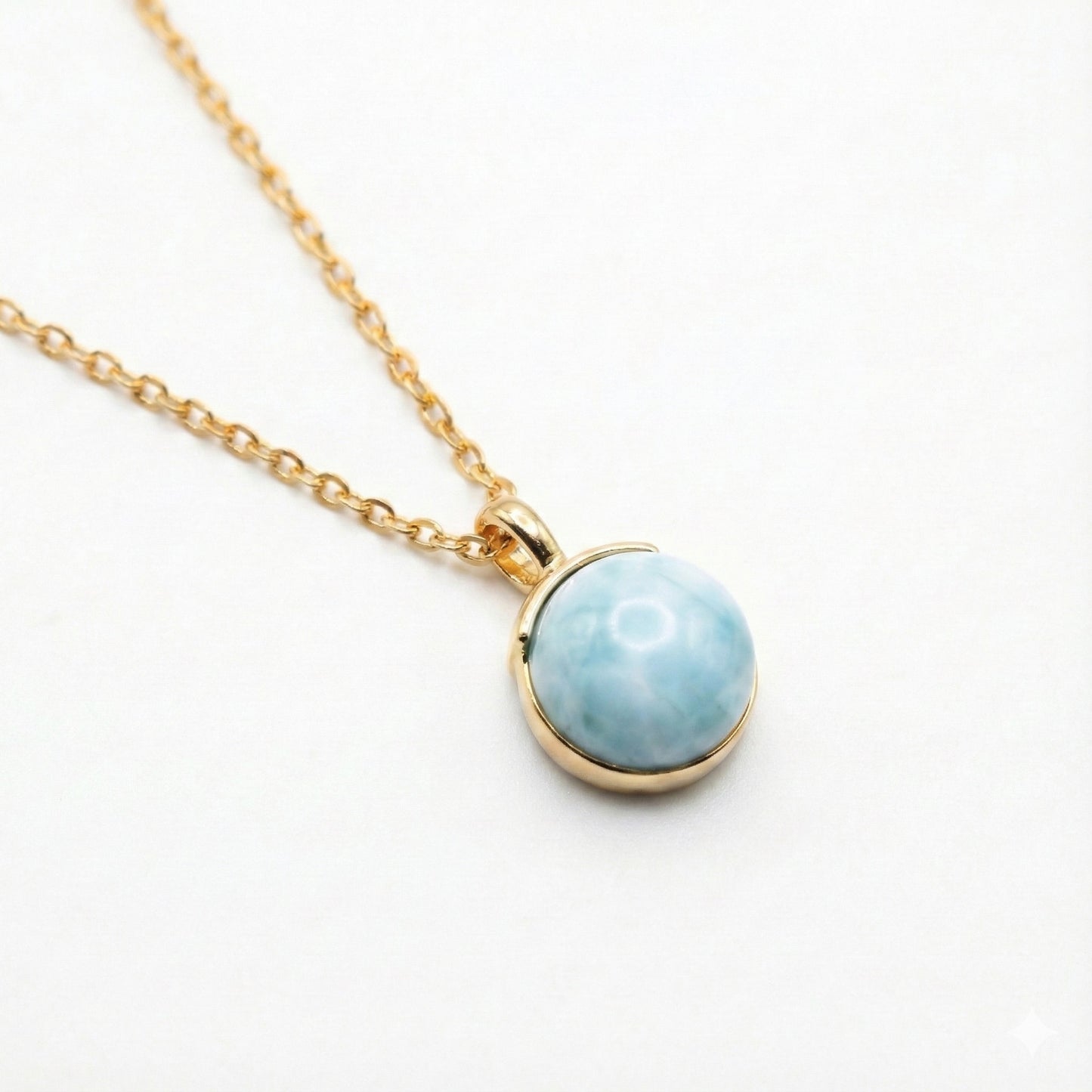 Gold chain necklace with round blue larimar pendant on white background