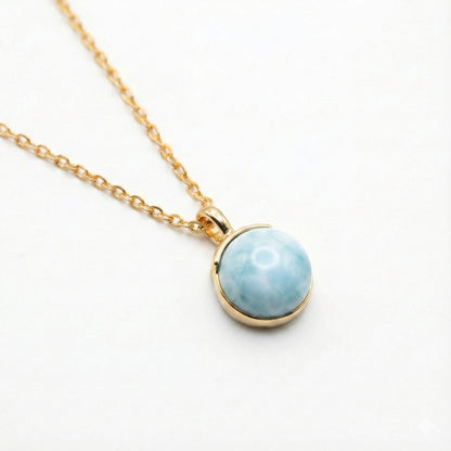 Gold chain necklace with round blue larimar pendant on white background