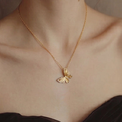 Gold butterfly necklace on a person wearing a black top against a neutral background