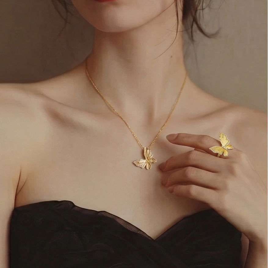 Woman wearing a gold butterfly necklace and ring against a neutral background